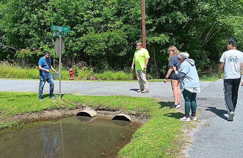 A group of Duke students measures the width of a drainage ditch near a street corner.